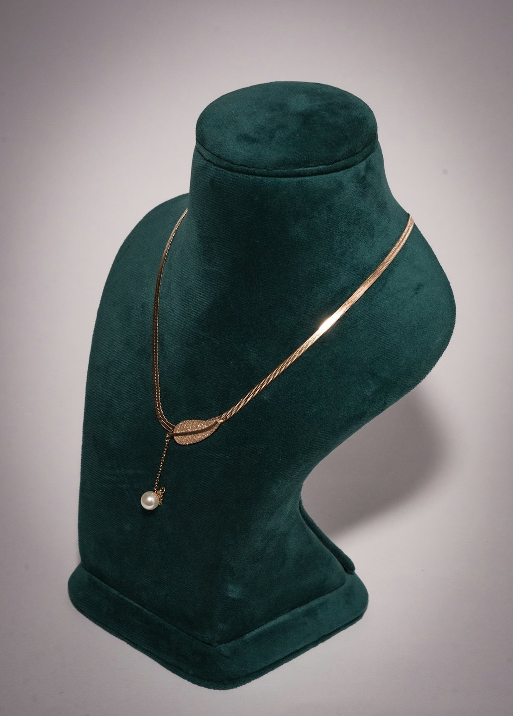 Gold leaf pendant necklace with a pearl on a display bust.