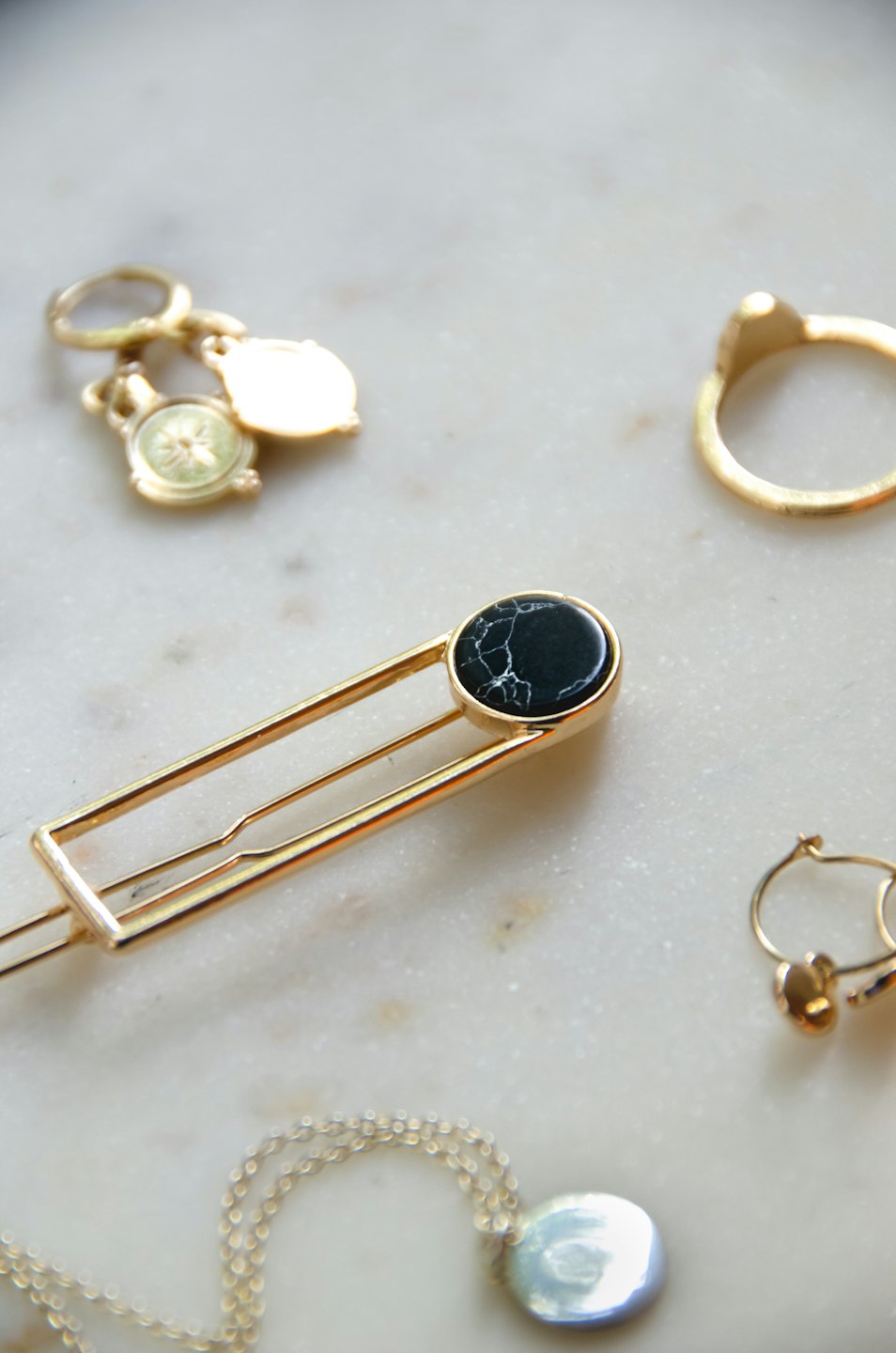 Gold jewelry on white marble, including a hair clip, earrings, ring, and necklace.