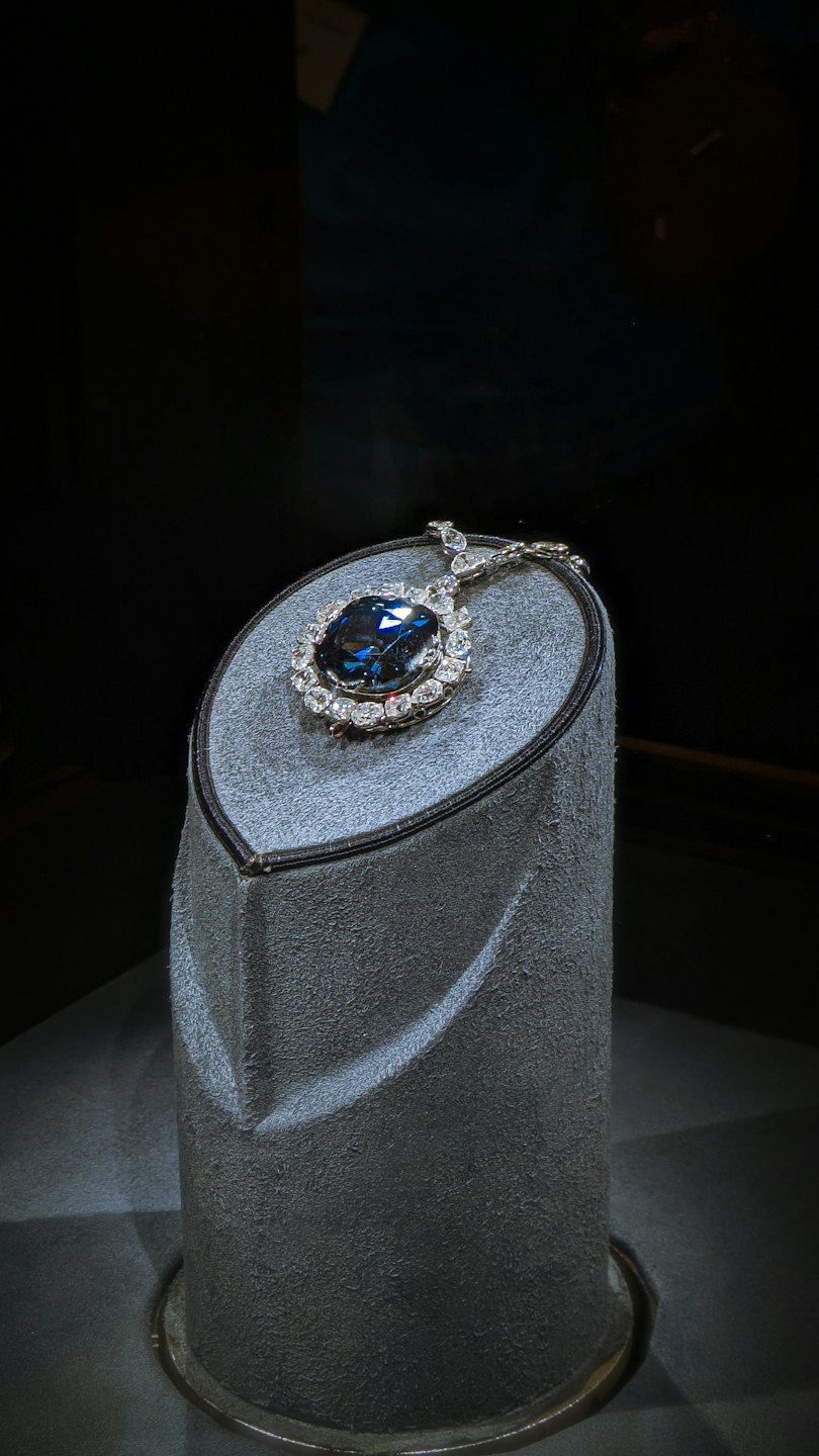 Dark blue gemstone pendant sits on a textured grey stand.