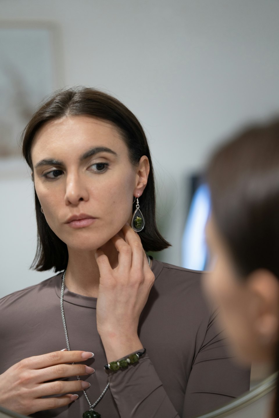 Woman admires her green stone earring and necklace in mirror.