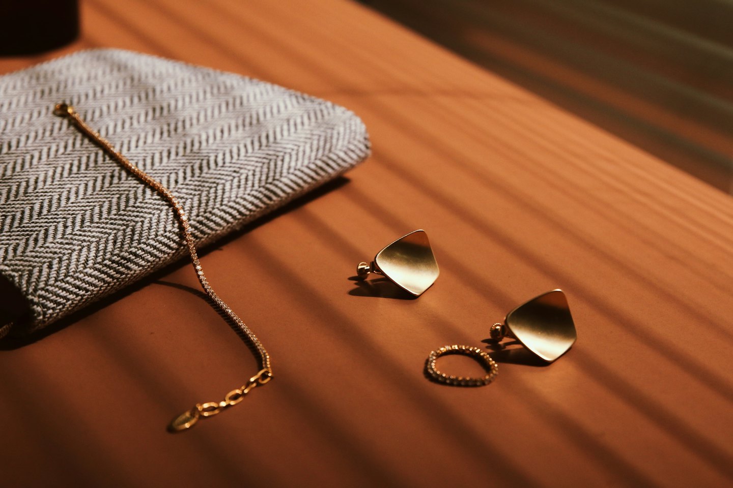 Gold geometric earrings, bracelet, and textured ring on brown surface.