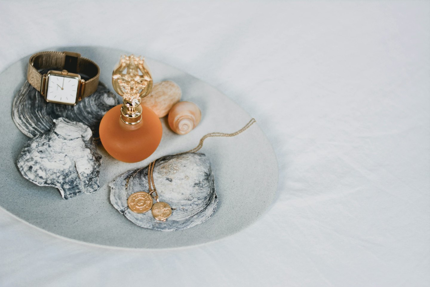 Gold jewelry, perfume bottle, and seashells on oval tray.
