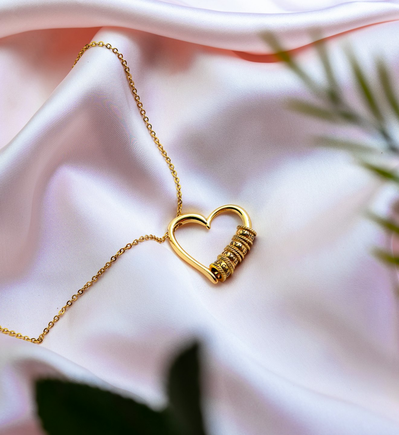 Gold heart necklace with engraved rings on pink satin.
